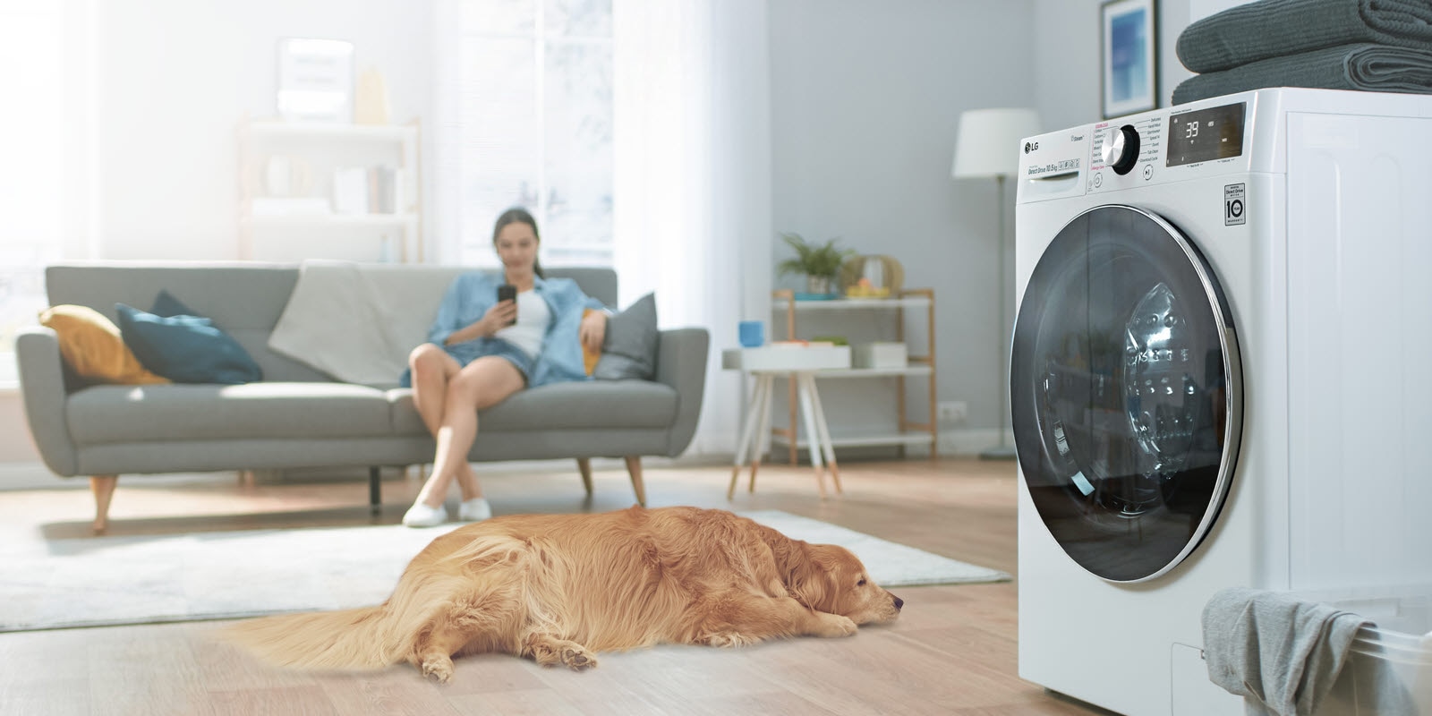 A side view of the washer sits to one side with a dog and a woman on her phone on the other side.