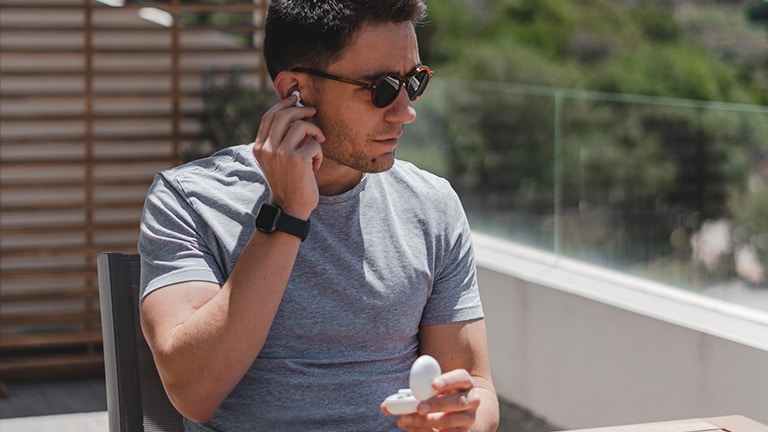 An image of a man with sunglasses taking out the earbud from his ear at a balcony on a daylight