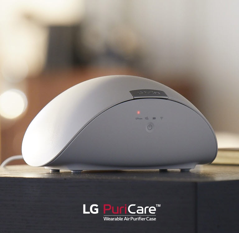 The LG PuriCare Wearable Air Purifier Case sits on a table. A red light is lit on the display.