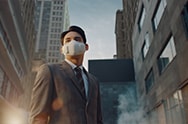 A video opens with a city under smog and then focuses on a road from above as cars drive in a circle but seem to slow down. The next shot shows a woman taking a large inhale through a mask and breathing in and out can be heard over the next few shots showing a subway train going by, people in a yoga class exhaling, people in an elevator inhaling. A black background and the words "As easy as breathing?" appears in the center and then disappears and the words "Now it can be." appear. The elevator doors open and the man wearing the LG PuriCare Wearable Air Purifier is in the front with people wearing normal cloth masks behind him. He taps the side of his mask to turn on the filters and the camera zooms inside the filter to see a mouth breathing comfortably inside. The video cuts to a stop light going from red to green and then the traffic in the street starts to speed up again from slow to fast. An airplane takes off into the sky, the sunsets, and the subway train flies by. A woman wearing the PuriCare mask on the streets turns to look up and then it cuts to a woman in a yoga class wearing the PuriCare mask stretching. A man standing on the street without a mask breathes in and the PuriCare mask appears around his face.  Next a white background and then the words "Technology that lets you breath easy". Finally the words disappear and the LG PuriCare Wearable Air Purifier logo ends the video.