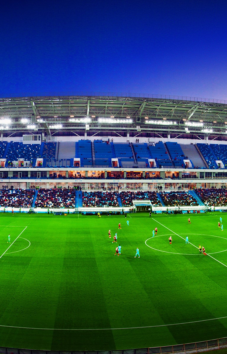 A wide-angled view of a football stadium with a full crowd and match in progress.