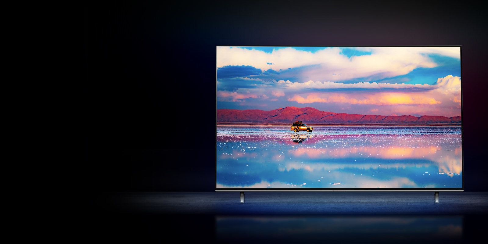 An LG NanoCell TV against a black background. The TV shows a car driving in front of a low mountain range in water that reflects the vivid sky.