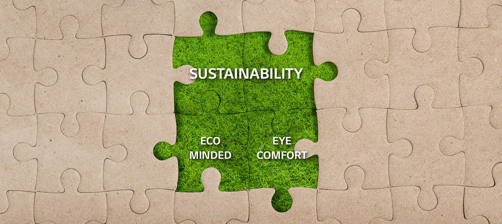 Four puzzle pieces in the middle of a kraft jigsaw puzzle are covered with a grass with texts of 'SUSTAINABILITY', 'ECO MINDED' and 'EYE COMFORT'.